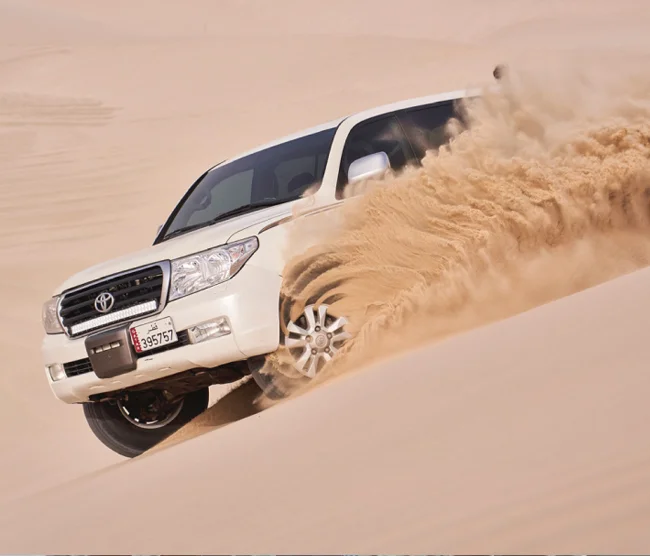 Tourists enjoying dune bashing in Qatar with 4x4 vehicles on golden sand dunes near the Inland Sea.