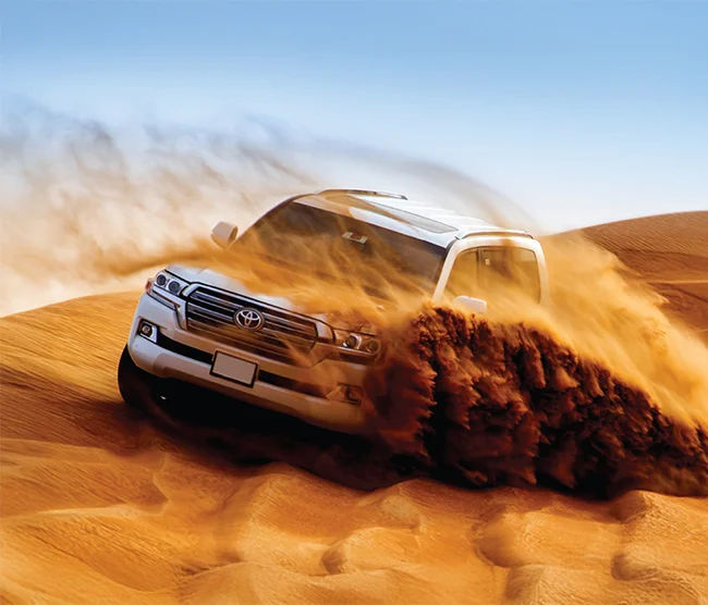 Dune-Bashin4×4 vehicle driving over golden sand dunes in Qatar’s desert during a thrilling dune bashing adventure.g