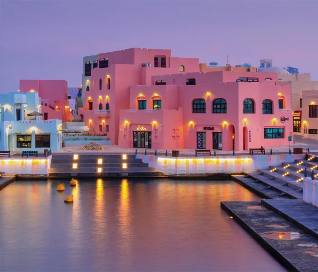 Colorful Mina District in Old Doha Port with vibrant buildings, waterfront promenade, and yachts in the background.