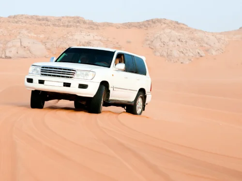 4x4 vehicle driving across high golden sand dunes during a desert safari in Qatar.